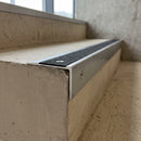Close-up of the 55mm aluminium front face and bonded black anti-slip insert with countersunk screw fixings on a concrete step edge