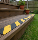 Black and yellow hazard-striped anti-slip GRP decking strip installed on a wooden garden decking step