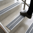 Foot stepping onto a concrete stair fitted with twin grey anti-slip inserts in an aluminium nosing