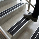 Foot stepping onto concrete stairs fitted with twin black anti-slip inserts in aluminium nosings