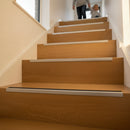 Aluminium stair nosing with black anti-slip insert installed on oak wood family home staircase UK — parent and child safely descending stairs