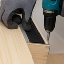 Hands screwing silver aluminium stair nosing into wooden step edge with cordless drill