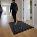 Person walking on black textured polypropylene entrance mat in modern home hallway with wooden floors