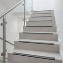 Heavy duty tile-in stair nosing installed on modern UK porcelain tiled staircase with glass balustrade - flush ceramic tile installation