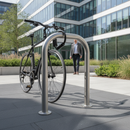 Polished stainless steel Sheffield-style cycle stand outside a modern glass office building, with a commuter bicycle locked to the hoop