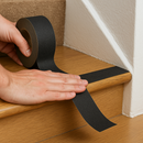 Person pressing black anti-slip tape down firmly on stair tread edge — self-adhesive application