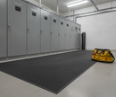 Black ribbed electrical safety matting laid in front of switchgear cabinets in a plant room with an electrician's tool bag