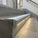 Matt silver end cap closing the open end of an LED stair nosing on a concrete stairwell step