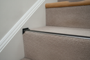 Matt black anodised aluminium stair nosing end cap fitted to a carpeted staircase edge in a UK home hallway