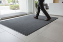 Grey mix heavy duty entrance barrier mat laid at a modern office reception entrance with a visitor walking across it
