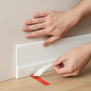 Person installing white self-adhesive skirting board trim with peel and press backing