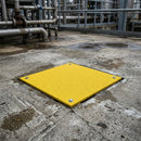 Yellow GRP hole cover anchored flush over an opening in a worn concrete industrial yard floor