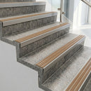 Raked back nosings with fawn ribbed inserts on pale concrete steps beside a glass balustrade