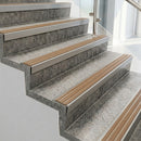 Raked back nosings with fawn ribbed inserts on pale concrete steps beside a glass balustrade