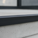 Close-up of black self-adhesive PVC stair nosing 50×48mm installed on step edge showing anti-slip grooves
