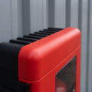 Close-up of the top corner of the red fire extinguisher cabinet showing the moulded cooling fins along the black rear shell, the rounded red door edge with rain beads, the shut line and the upper hinge against grey steel cladding