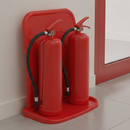 Red plastic double fire extinguisher floor stand holding two fire extinguishers positioned near a fire exit door in a corridor