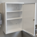 Interior of the empty first aid cabinet with its door open, showing two fitted white steel shelves, three empty compartments and pre-drilled keyhole wall-mounting holes