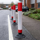 Row of red and white flexible traffic delineator posts bolted to tarmac separating a service lane in a business park car park