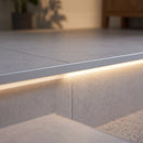 Close-up of the matt silver NLD nosing flush with a porcelain tread, LED glow washing the riser below