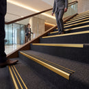 Gold anodised aluminium stair nosing with twin black rubber inserts on a plain studio background