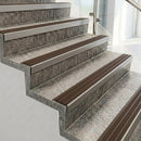 Raked back nosings with granite brown ribbed inserts on pale concrete steps beside a glass balustrade