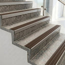 Raked back nosings with granite brown ribbed inserts on pale concrete steps beside a glass balustrade