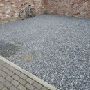 Grey gravel off-road parking area beside a brick garage with the honeycomb grid visible beneath the stone