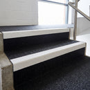Black GRP stair tread cover with white nosing fitted over concrete steps in a commercial stairwell