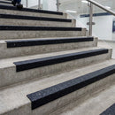 Black GRP nosings on concrete stairs in a modern building, glass balustrade and stainless handrail alongside