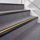 Satin black double insert chevron stair nosing with yellow inserts fitted on grey carpeted stairs