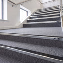 Heavy duty rake back aluminium stair nosing with black insert in bright polished finish fitted on a stair with grey contract carpet