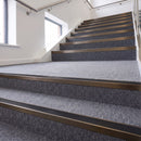Heavy duty rake back aluminium stair nosing with black insert in dark bronze finish fitted on a stair with grey contract carpet