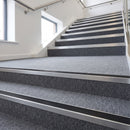 Heavy duty rake back aluminium stair nosing with black insert in mill finish finish fitted on a stair with grey contract carpet