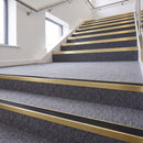 Heavy duty rake back aluminium stair nosing with black insert in satin gold finish fitted on a stair with grey contract carpet