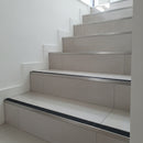 Heavy-duty wide 35mm aluminium stair nosing with black anti-slip insert installed full-width on porcelain tile staircase UK — low angle view