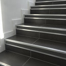 Heavy-duty wide 35mm aluminium stair nosing with grey anti-slip insert installed full-width on dark porcelain tile staircase UK — low angle view