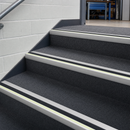 Black silicon carbide stair nosing fitted across the full width of every step on a grey carpeted commercial staircase, glow strip along the nose