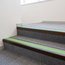 Dark bronze aluminium stair nosing with Apple Green insert fitted to grey carpet tile on an academy school stairwell