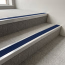 Mill finish aluminium stair nosing with Dark Blue insert fitted to pale grey carpet tile on a college corridor stair