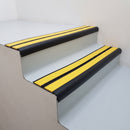 Satin black aluminium bullnose stair nosing with twin yellow inserts fitted on a public building stairwell step