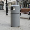 Dark grey 90 litre hooded top litter bin standing on grey paving in a pedestrianised town centre, beside a wooden slatted bench and a black cast-iron street lamp, with blurred shopfronts behind