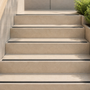 Slim black inserts recessed into sandy beige outdoor steps in sunlight, shrub at the top right
