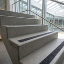 Pale concrete staircase beside a glazed wall, each tread inset with a dark anti-slip strip