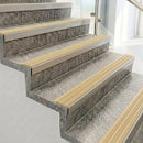 Raked back nosings with ivory ribbed inserts on pale concrete steps beside a glass balustrade