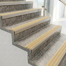 Raked back nosings with ivory ribbed inserts on pale concrete steps beside a glass balustrade