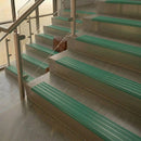 Brass stair nosings with jade green ribbed inserts on pale stone steps beside a glass balustrade