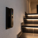Handheld remote dimmer for LED stair lighting on a hallway wall plate beside a lit tiled staircase