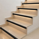 Black matt aluminium LED stair nosing profiles illuminating cream stone steps with warm white LED light