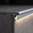 Close-up of aluminium LED stair nosing at a tiled step edge, LED strip in the channel lighting the riser
